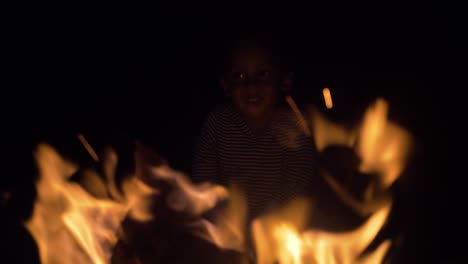 A-close-up-of-a-young-mixed-raced-child's-face-as-he-leans-and-looks-into-the-flames-of-a-camp-fire