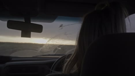 Adult-female-rear-view-driving-on-road-trip-looking-through-dirty-windshield-at-dusk