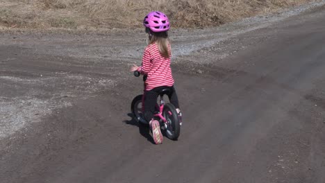 Handheld,-slow-motion-shot-of-a-little-girl-cycling-on-a-gravel-road,-on-the-finnish-countryside,-on-a-sunny-spring-day,-in-Vaasa,-Ostrobothnia,-Finland