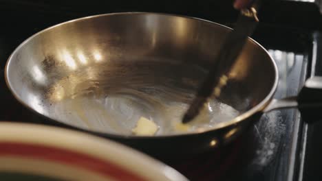 Melting-Sliced-Of-Butter-In-A-Low-Heated-Frying-Pan-Using-A-Metal-Knife---Close-Up-Shot