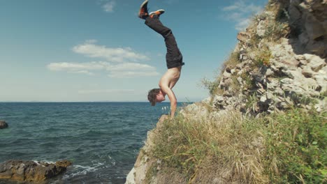 Young-caucasian-male-does-an-extended-handstand-on-a-cliffside-overlooking-the-ocean