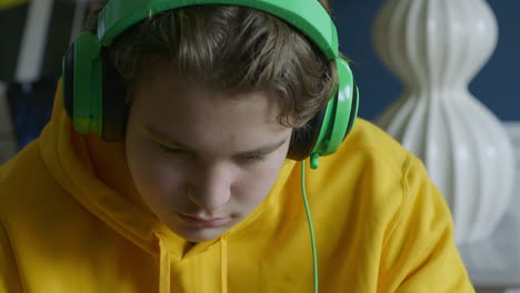 Teen-boy-wearing-headphones-while-working-at-the-table-nods-along-to-the-beat,-close-up