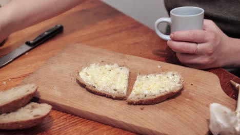 Woman's-hands-take-a-crystal-glass-with-vodka,-a-cut-slice-of-bread-smeared-with-butter-and-garlic-lies-on-a-chopping-board