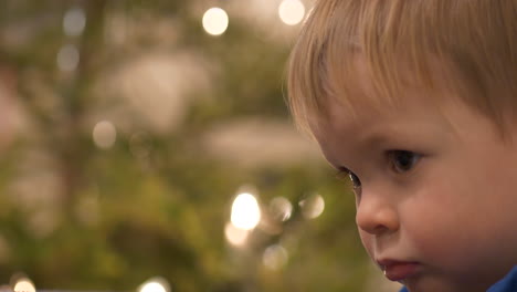 Tired-toddler-with-empty-eyes-in-front-of-Christmas-Tree,-Close-up
