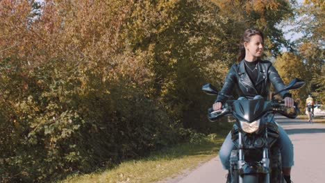 Driving-in-front-of-smiling,-talking-European-Female-motorbiker-wearing-leather-jacket-driving-on-road-passes-cyclists
