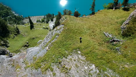 Revealing-aerial-shot-of-a-woman-hiking-on-the-edge-of-a-mountain-with-a-beautiful-blue-lake-in-the-background