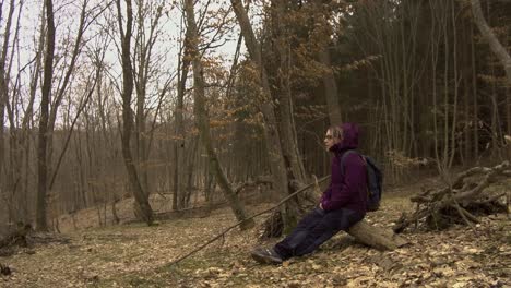 Low-angle-view-of-woman-resting-on-a-fallen-tree-in-the-woods