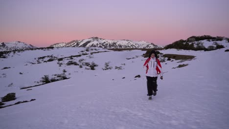 Slow-motion-shot-of-a-woman-trekking-in-the-snow-with-a-beautiful-sunset-behind