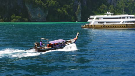 A-traditionally-designed-tourist-boat-taking-people-back-to-the-beach-of-Thailand,-passing-a-tourist-yacht---wide-rolling