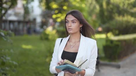 Young-business-woman-walking-and-reading-her-notebook-in-a-park