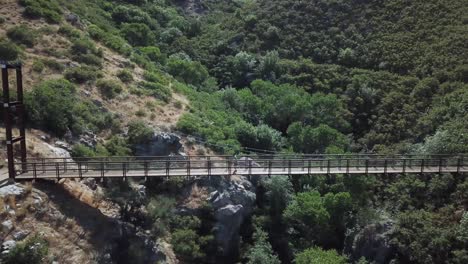 Drone-Shot-following-an-active-man-running-on-an-outdoor-hanging-suspension-bridge-above-Bear-Canyon-in-Draper-City,-Utah-2
