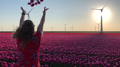 Girl-in-field-of-tulips-and-wind-turbines-throwing-flowers-in-air,-slow-motion