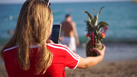 Female-tourist-with-blonde-hair-enjoy-taking-photo-of-refreshing-pineapple-cocktail-drink-on-beach-in-Turkey---Mid-shot