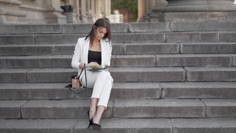 A-professional-young-woman-in-business-suit-makes-notes-in-her-diary-was-sitting-on-the-steps