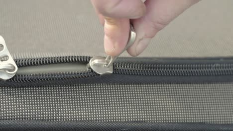 Hand-pulling-metal-zip-to-open-suitcase-close-up-detail