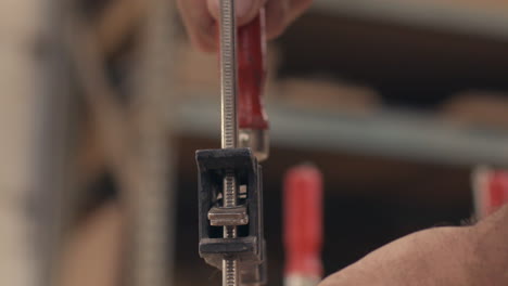 Craftsman-screws-down-vise-clamp-onto-wood-in-shop,-close-up-slow-motion