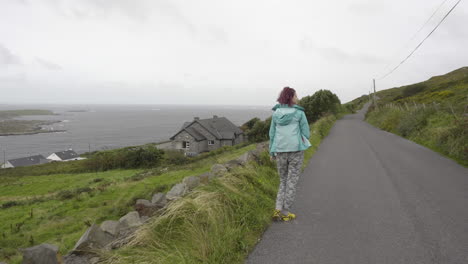 Tracking-shot-of-girl-walking-on-a-sky-road-looking-at-Atlantic-Ocean-and-the-coast-of-Ireland-in-4K