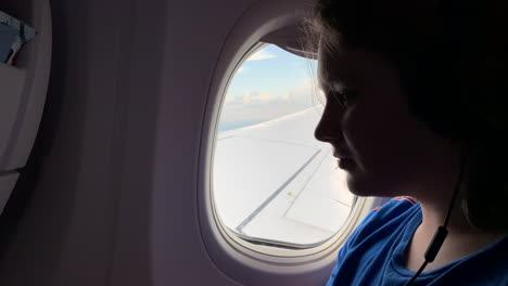 Teen-boy-on-an-airplane-looks-out-the-window-and-then-down-at-his-iPhone