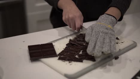 A-young-girl-cuts-up-dark-chocolate-before-melting-it-for-millionaire-shortbread-cookies-while-wearing-safety-gloves-6