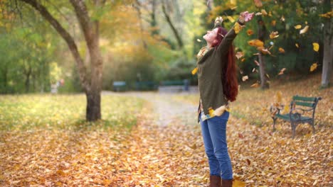Slow-Motion:-Beautiful-young-redhead-woman-standing-in-a-park-in-autumn-with-leaves-falling-down-around-her