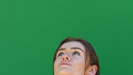 Static-close-up-shot-of-a-brunette-lady's-face-from-the-nose-up-in-front-of-a-green-chroma-key-backdrop-looking-at-the-sky-with-excitement-and-laughter