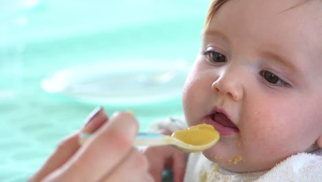 A-mother's-hand-carrying-a-spoon-full-of-baby-food-is-twirled-around-just-before-it-enters-into-the-toddlers-mouth,-Close-up-shot-slow-motion