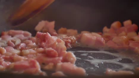 Close-up-on-pieces-of-greasy,-bubbling,-steaming-bacon-bits-in-hot-frying-pan