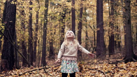Young-girl-in-throws-fall-leaves-in-air-in-autumn-forest,-slow-motion