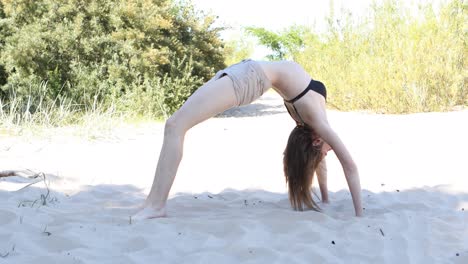Young-woman-is-making-backbend-exercise-on-beach-in-sunny-summer-day
