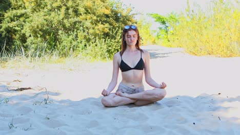 Meditating-woman-is-sitting-in-lotus-pose-on-sandy-beach-in-summer-day