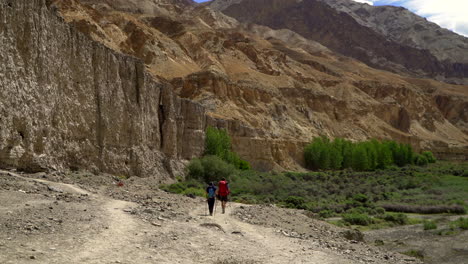 Dos-Personas,-Excursionistas-Mochileros-Caminando-Por-Un-Camino-En-Las-Montañas-En-Un-Día-Muy-Caluroso,-Mientras-El-Aire-Vibra-A-Su-Alrededor