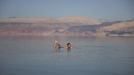 Traveler-swimming-in-the-dead-sea,-mountains-background,-clear-sky,-sunset,-static-shot