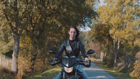 Beautiful-european-young-lady-riding-her-motorbike-wearing-leather-jacket-driving-On-road-captured-from-back-of-car