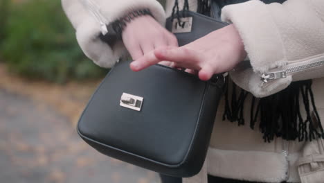 Close-up-of-a-black-purse-around-a-woman's-waist-wearing-a-white-warm-coat