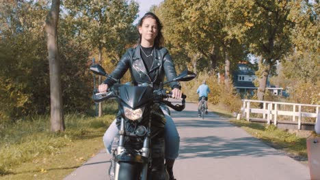 Vista-Frontal-De-La-Hermosa-Chica-Europea-Pelirroja-Que-Habla-Conduciendo-Motocicleta-En-La-Carretera-Pasando-Bicicletas