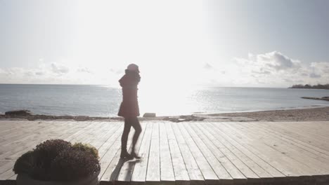 A-Woman-Walking-Along-The-Lakeshore-With-Beautiful-Morning-Sunlight-Glimmering-Beyond-The-Water-Surface---Medium-Shot