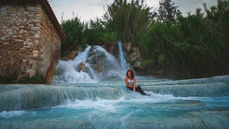 4K-UHD-Cinemagraph---seamless-video-loop-of-a-young-woman-sitting-in-front-of-a-thermal-hot-springs-waterfall-in-Saturnia,-Italy