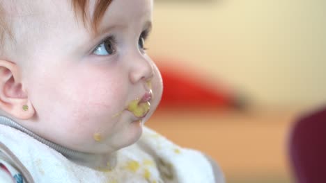 After-taking-a-bite-of-baby-food-from-its-mother,-the-baby-gazes-up-at-its-mother-with-food-still-on-its-face,-close-up-shot