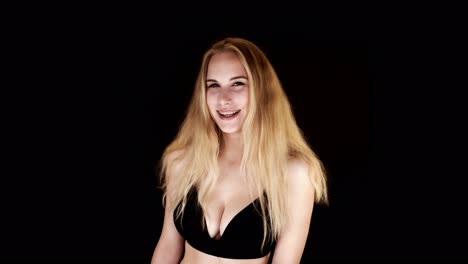Lit-from-below,-a-busty-blonde-woman-looks-directly-at-the-camera,-laughing-and-shrugging-suggestively