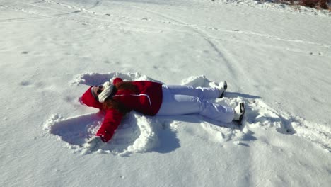A-slow-motion-side-view-of-a-girl-making-a-snow-angel-in-the-snow-during-a-bright-and-sunny-winter-afternoon-outdoors