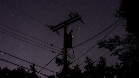 Ein-Zeitraffer-Der-Sterne,-Die-Sich-Am-Himmel-Hinter-Einem-Silhouettierten-Vorstadt-Telefonmast-Und-Stromleitungen-Und-Bäumen-Am-Nachthimmel-Drehen