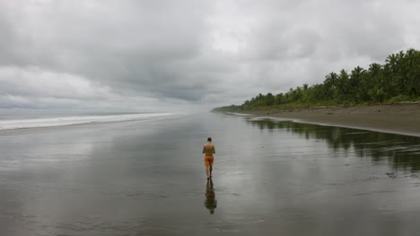 Aerial-follows-a-young-man-that-walks-on-an-empty-beach,-Colombia