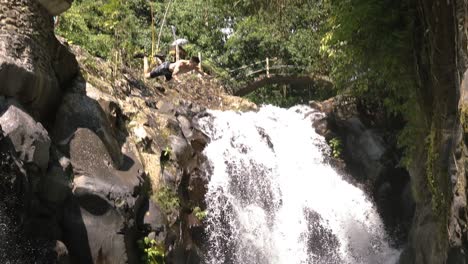 Slow-Motion-shot-of-an-american-tourist-cliff-jumping-and-doing-a-gainer-off-of-a-cliff-into-a-pool-of-water-at-AlingAling-Waterfall-in-Bali,-Indonesia