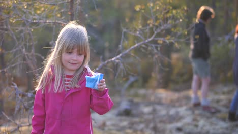 Static,-slow-motion-shot-of-a-little-blonde-girl-smiling-and-showing-her-toy,-in-a-finnish-forest,-on-a-sunny-spring-day,-in-Vaasa,-Ostrobothnia,-Finland