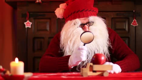 Santa-Claus-With-Magnifying-Glass-Inspects-Apples-On-A-Wooden-Toy-Truck-1