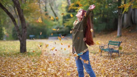 4K-Slow-Motion:-Beautiful-young-redhead-woman-standing-in-a-park-in-autumn-with-leaves-falling-down-around-her