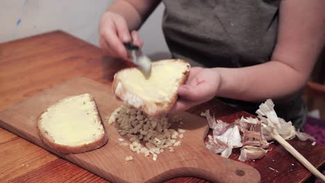 Woman's-hands-butter-a-slice-of-bread,-the-chopped-garlic-lies-on-a-chopping-board