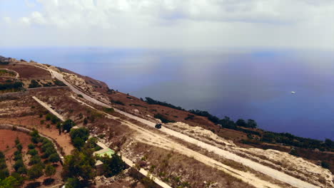 Aerial-Panorama-Of-Single-ATV-Driving-Along-Cliff-Edge-Road,-Dramatic-Ocean-Backdrop