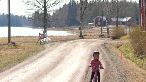 Handheld,-slow-motion-shot-of-a-little-girl-cycling-on-a-gravel-road,-on-the-finnish-countryside,-on-a-sunny-spring-day,-in-Vaasa,-Ostrobothnia,-Finland-1