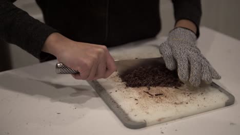 A-young-Korean-girl-cuts-up-dark-chocolate-before-melting-it-for-millionaire-shortbread-cookies-while-wearing-safety-gloves